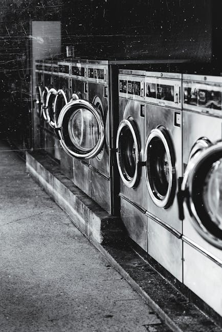 A row of industrial washing machines in an urban laundromat, showcasing steel finish.